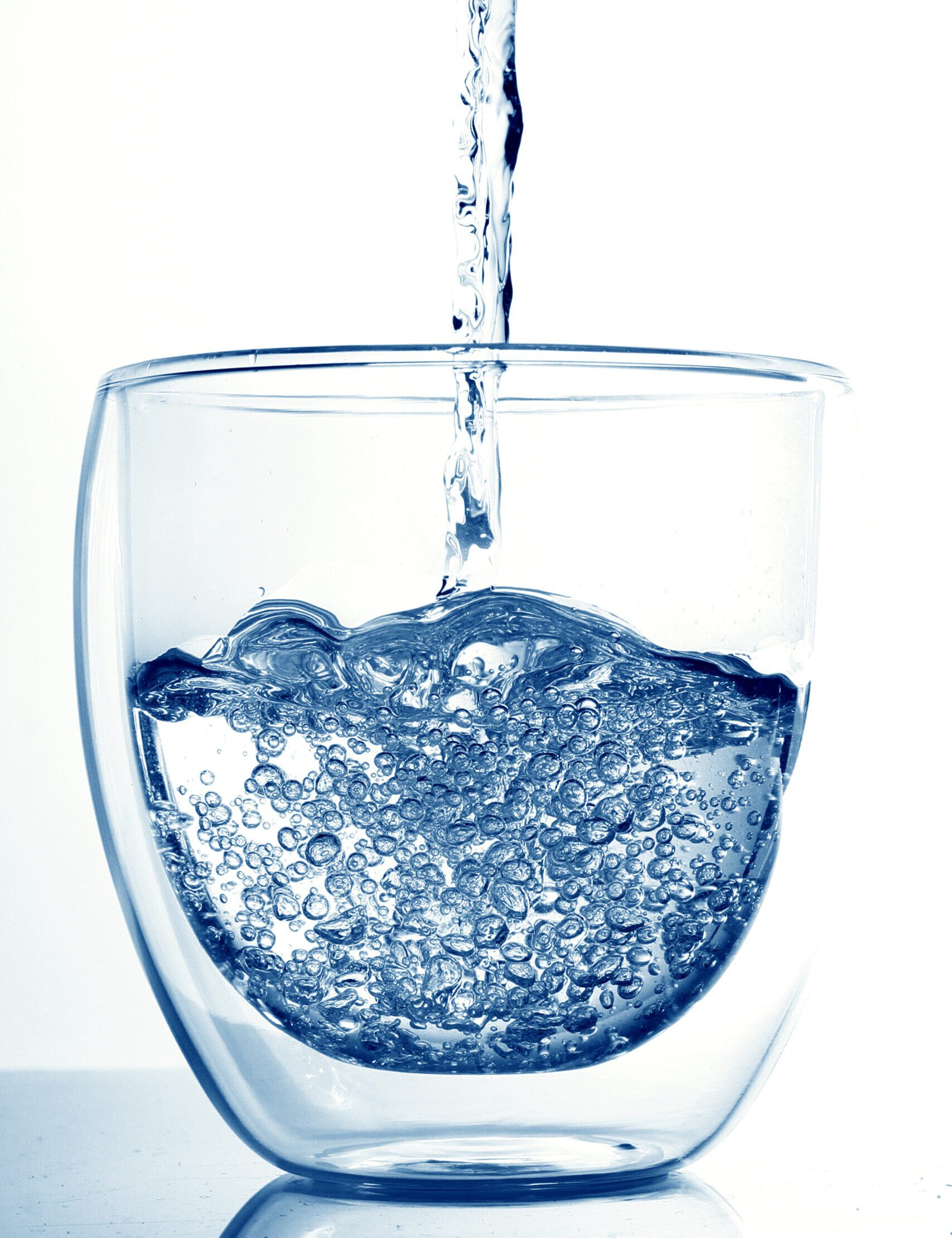 Ein Glas wird mit klarem Wasser gefüllt, Blasen steigen auf. Kühles Blau dominiert die Szene.