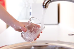 Nahaufnahme eines Wasserhahns, der Wasser in ein von einer Hand gehaltenes Glas in heller Küche füllt.