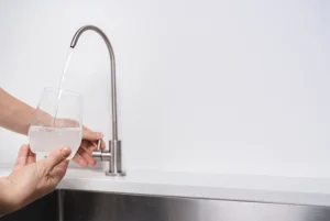 Eine Hand füllt ein Glas mit Wasser aus einem eleganten, gebogenen Edelstahl-Wasserhahn in moderner Küche.