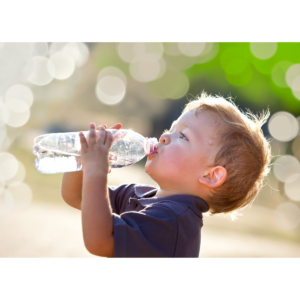 Ein Kind trinkt aus einer durchsichtigen Wasserflasche im Freien, umgeben von unscharfem Hintergrund.