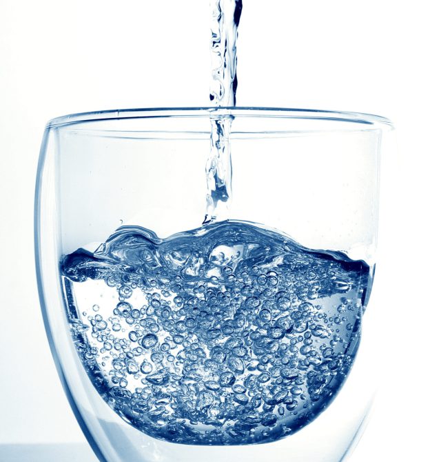 close-up-water-pouring-glass-against-white-background
